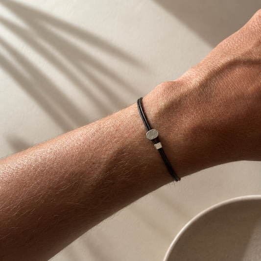 Close-up of a wrist wearing a black bracelet with a silver charm on a neutral background