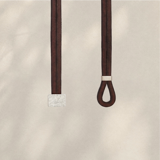 Two dark brown leather straps hanging against a warm beige textured background, one with a square textured silver-toned end and the other with a small silver-toned band near a looped end.