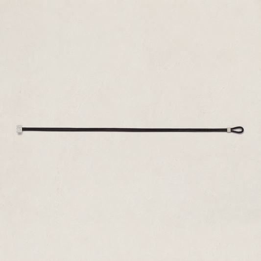 A minimalist black leather strap with silver metal hardware, displayed horizontally against a textured off-white background.