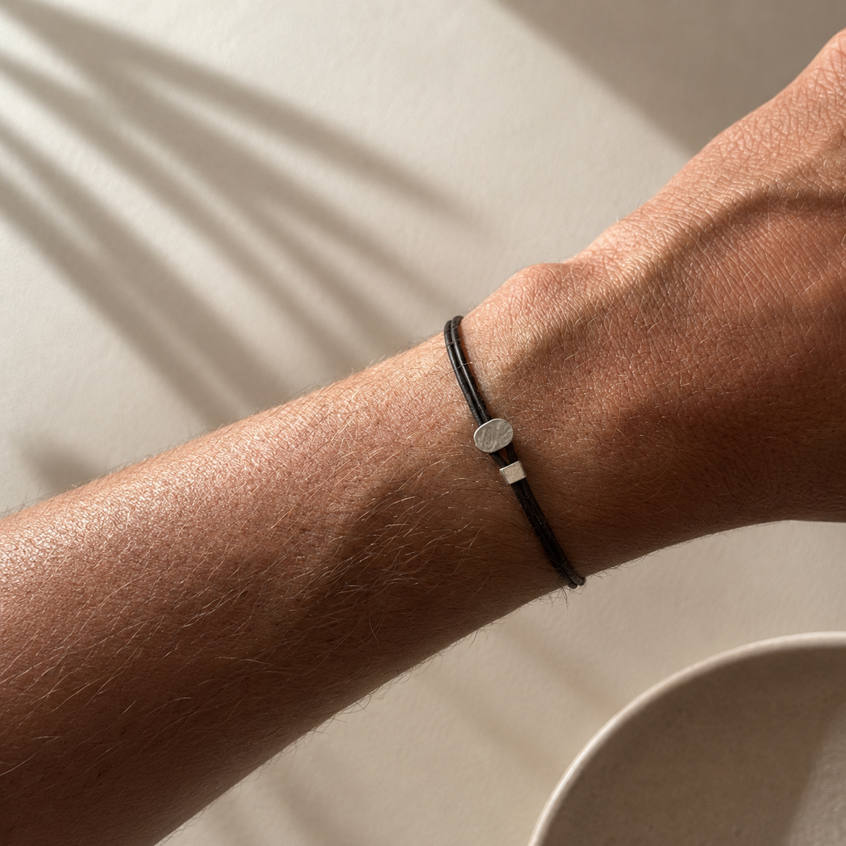 Close-up of a wrist wearing a black bracelet with a silver charm on a neutral background