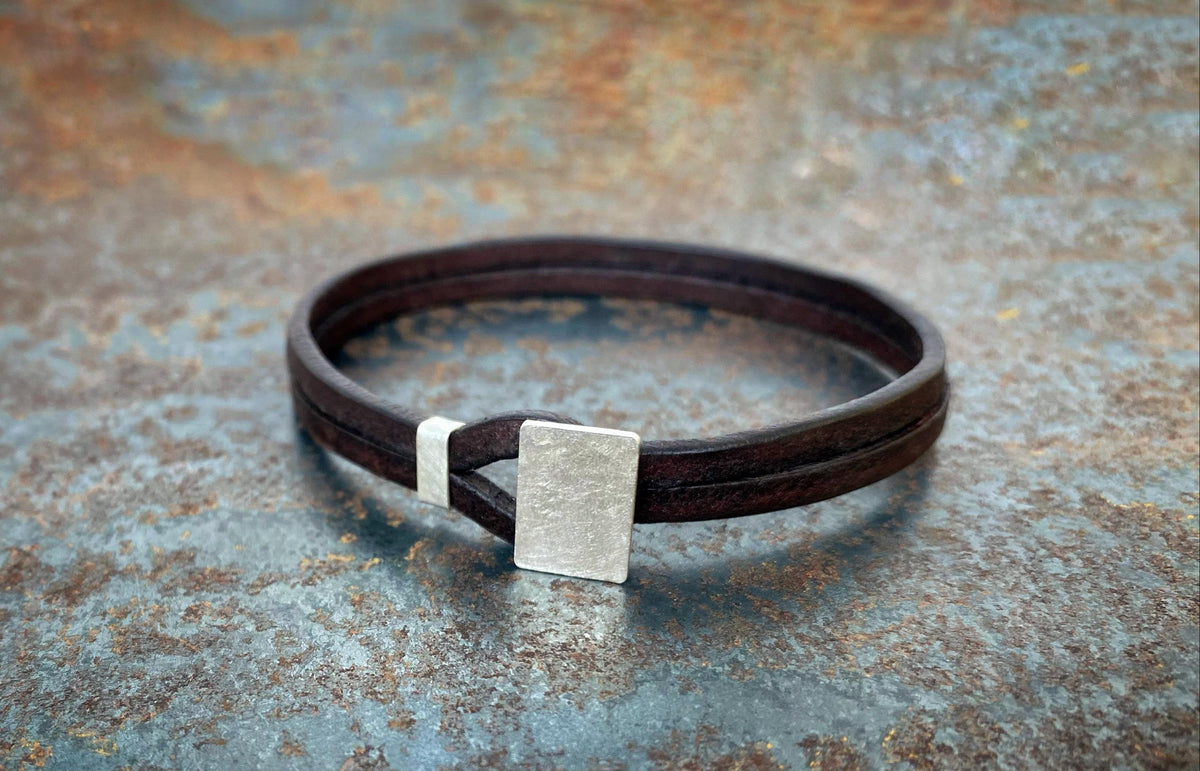 Brown leather bracelet with a silver square clasp on a textured surface