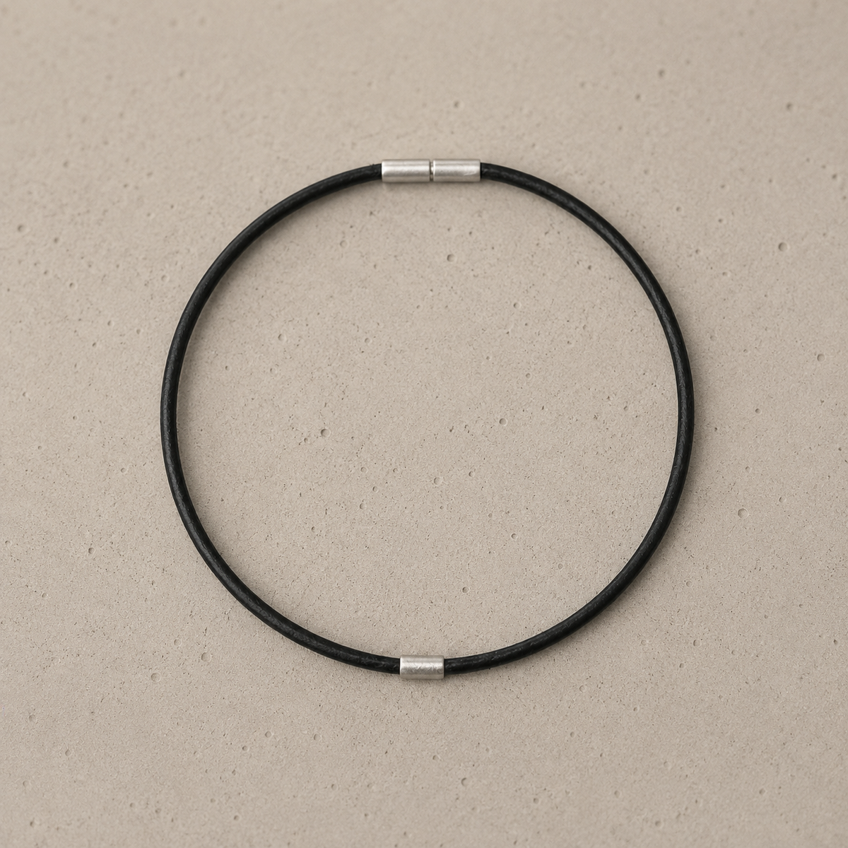 A minimalist black circular leather anklet with silver bayonet clasp and 925 stirling silver element, displayed on a textured beige background.