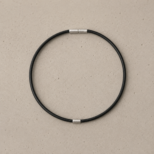 A minimalist black circular leather anklet with silver bayonet clasp and 925 stirling silver element, displayed on a textured beige background.
